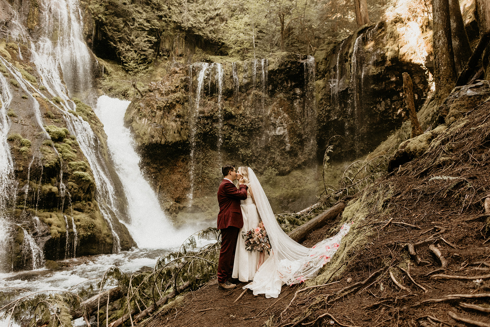 bride and groom kissing waterfall forest landscape