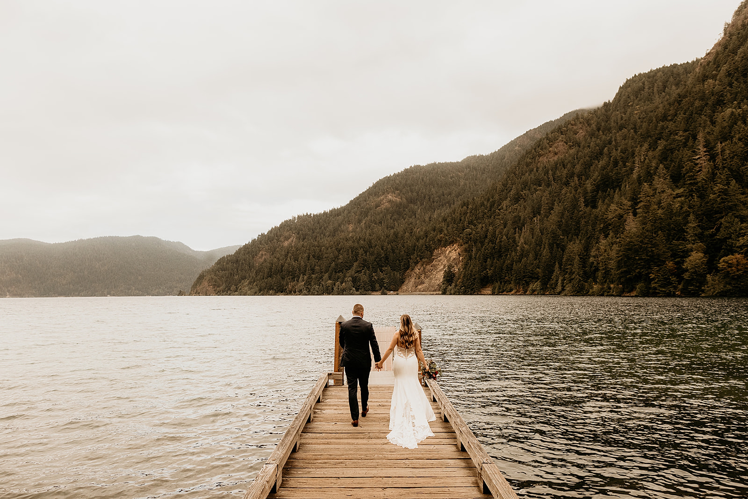 bride and groom walking together on dock lake forest view