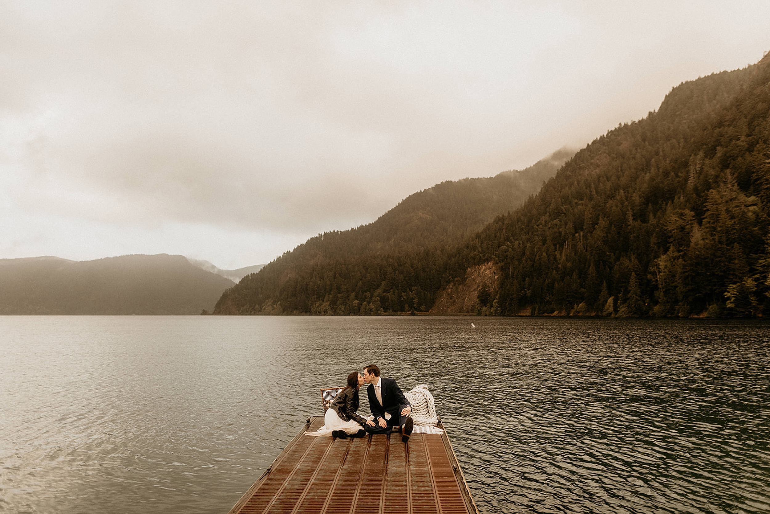 bride and groom kissing on dock lake valley landscape 